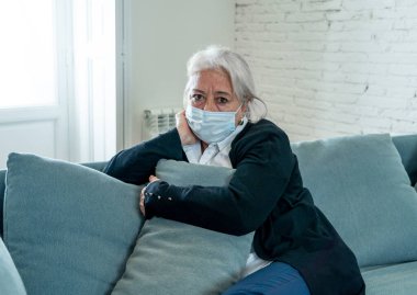 Yalnız, koruyucu maskeli yaşlı dul bir kadın evde yalnız başına ağlıyor, üzgün ve endişeli bir koca ve aile COVID-19 'da kayıp, tecrit, sosyal mesafeler ve akıl sağlığı.