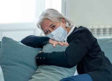 Yalnız, koruyucu maskeli yaşlı dul bir kadın evde yalnız başına ağlıyor, üzgün ve endişeli bir koca ve aile COVID-19 'da kayıp, tecrit, sosyal mesafeler ve akıl sağlığı.