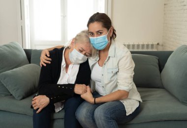 Depresyondaki anne ve kızı tıbbi maske takıp ağlıyorlar ve Coronavirus 'la savaşan sevdiklerinin yasını tutuyorlar. COVID-19 salgınından etkilenen insanlar ve aileler.