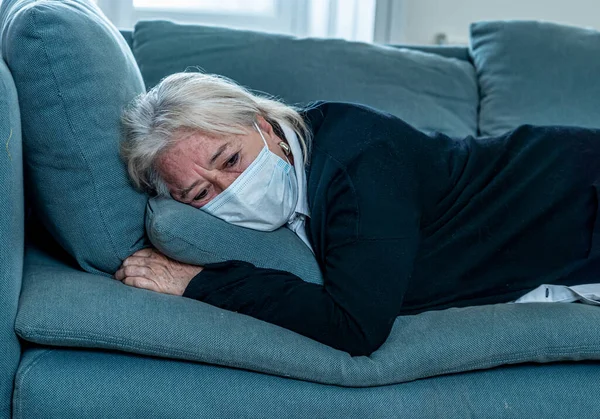 Lonely depressed senior widow woman with protective mask crying on couch isolated at home, sad and worried missing husband and family in COVID-19 death, lockdown, social distancing and Mental health.