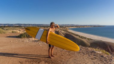 Çekici Avustralyalı olgun sörfçü gün batımında plajda kaliteli sörf tahtasıyla. Son sınıf öğrencisi sörf yapmaya döndüğü için mutlu. Açık hava sporları, aktif yaşlılar ve emeklilik hayatı..
