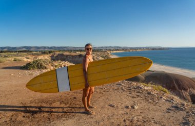 Çekici Avustralyalı olgun sörfçü günbatımında kaliteli sörf tahtasıyla. 50 'li yaşlardaki zinde kadın sörf yapmaya döndüğü için mutlu. Açık hava sporları, aktif yaşlılar ve emeklilik hayatı..