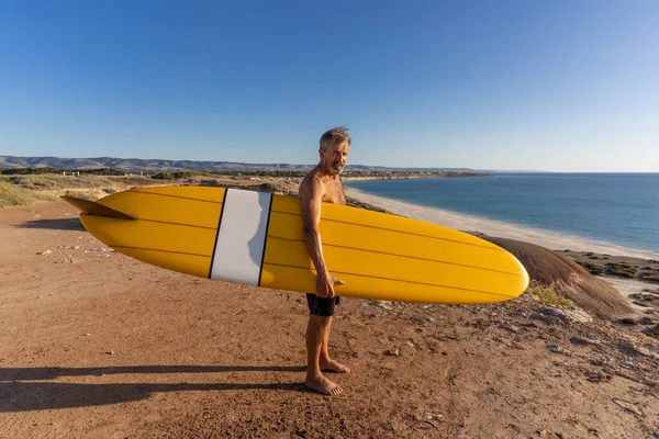 Çekici Avustralyalı olgun sörfçü gün batımında plajda kaliteli sörf tahtasıyla. Son sınıf öğrencisi sörf yapmaya döndüğü için mutlu. Açık hava sporları, aktif yaşlılar ve emeklilik hayatı..