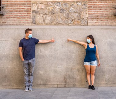 Korumacı yüz maskeleri takan erkek ve kadın birbirlerinden 2 metre uzakta duruyorlar. Sosyal mesafeyi koronavirüsün yayılmasını önlüyorlar. COVID-19 hastalıkların korunmasının kavramsal görüntüsü ve Yeni Normal.