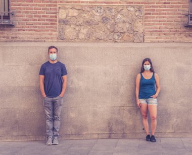 Korumacı yüz maskeleri takan erkek ve kadın birbirlerinden 2 metre uzakta duruyorlar. Sosyal mesafeyi koronavirüsün yayılmasını önlüyorlar. COVID-19 hastalıkların korunmasının kavramsal görüntüsü ve Yeni Normal.