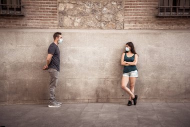 Korumacı yüz maskeleri takan erkek ve kadın birbirlerinden 2 metre uzakta duruyorlar. Sosyal mesafeyi koronavirüsün yayılmasını önlüyorlar. COVID-19 hastalıkların korunmasının kavramsal görüntüsü ve Yeni Normal.