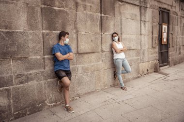 Korumacı yüz maskeleri takan erkek ve kadın birbirlerinden 2 metre uzakta duruyorlar. Sosyal mesafeyi koronavirüsün yayılmasını önlüyorlar. COVID-19 hastalıkların korunmasının kavramsal görüntüsü ve Yeni Normal.