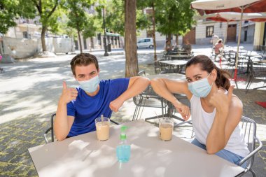 Yeni dirsek stili bir kahve dükkanında cerrahi koruyucu yüz maskesi takan arkadaşlar Coronavirus New Normal 'da halka açık yerlerde vakit geçiriyorlar. COVID-19 Salgın Önleme.