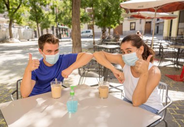 Yeni dirsek stili bir kahve dükkanında cerrahi koruyucu yüz maskesi takan arkadaşlar Coronavirus New Normal 'da halka açık yerlerde vakit geçiriyorlar. COVID-19 Salgın Önleme.