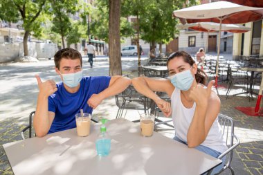 Yeni dirsek stili bir kahve dükkanında cerrahi koruyucu yüz maskesi takan arkadaşlar Coronavirus New Normal 'da halka açık yerlerde vakit geçiriyorlar. COVID-19 Salgın Önleme.
