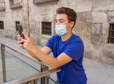 COVID-19 salgını. Şehirdeki genç adam koruyucu cerrahi maske takıyor ve arkadaşlarını ve ailesini cep telefonuyla arıyor. Yeni Normal ve zorunlu yüz maskesi kullanımında bağlı kalın.