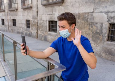 COVID-19 salgını. Şehirdeki genç adam koruyucu cerrahi maske takıyor ve arkadaşlarını ve ailesini cep telefonuyla arıyor. Yeni Normal ve zorunlu yüz maskesi kullanımında bağlı kalın.