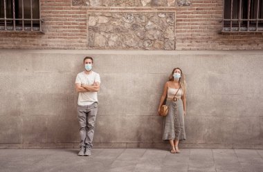 Yüz maskesi takan erkek ve kadın birbirlerinden 2 metre uzakta duruyorlar. Sosyal mesafeyi koruyorlar. Fiziksel temastan, enfeksiyondan ve koronavirüsün yayılmasından kaçınıyorlar. COVID-19 sağlık protokolleri ve Yeni Normal.