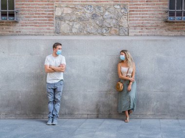 Yüz maskesi takan erkek ve kadın birbirlerinden 2 metre uzakta duruyorlar. Sosyal mesafeyi koruyorlar. Fiziksel temastan, enfeksiyondan ve koronavirüsün yayılmasından kaçınıyorlar. COVID-19 sağlık protokolleri ve Yeni Normal.