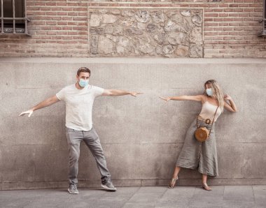 Yüz maskesi takan erkek ve kadın birbirlerinden 2 metre uzakta duruyorlar. Sosyal mesafeyi koruyorlar. Fiziksel temastan, enfeksiyondan ve koronavirüsün yayılmasından kaçınıyorlar. COVID-19 sağlık protokolleri ve Yeni Normal.