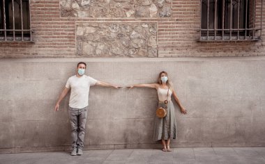 Yüz maskesi takan erkek ve kadın birbirlerinden 2 metre uzakta duruyorlar. Sosyal mesafeyi koruyorlar. Fiziksel temastan, enfeksiyondan ve koronavirüsün yayılmasından kaçınıyorlar. COVID-19 sağlık protokolleri ve Yeni Normal.