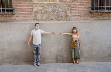 Yüz maskesi takan erkek ve kadın birbirlerinden 2 metre uzakta duruyorlar. Sosyal mesafeyi koruyorlar. Fiziksel temastan, enfeksiyondan ve koronavirüsün yayılmasından kaçınıyorlar. COVID-19 sağlık protokolleri ve Yeni Normal.