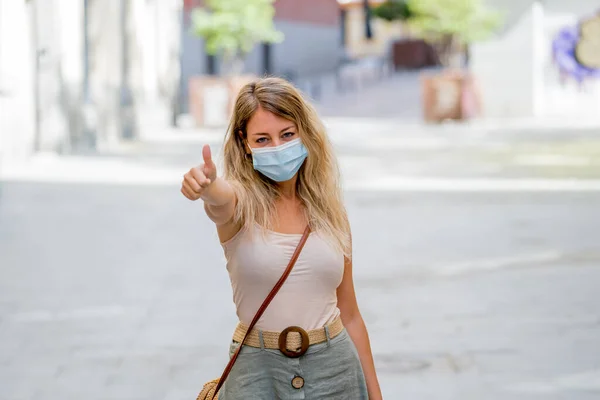 Young woman wearing protective face mask outdoors in city street. Positive image of New Normal life after COVID-19 and health protocols to avoid infections and the virus spread in public spaces.