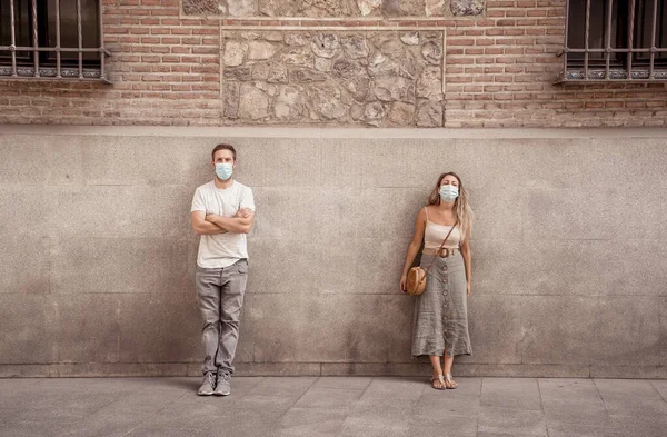 Yüz maskesi takan erkek ve kadın birbirlerinden 2 metre uzakta duruyorlar. Sosyal mesafeyi koruyorlar. Fiziksel temastan, enfeksiyondan ve koronavirüsün yayılmasından kaçınıyorlar. COVID-19 sağlık protokolleri ve Yeni Normal.