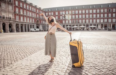 Korunaklı yüz maskesi takan genç turist kadın Coronavirus salgını sonrası İspanya Plaza Belediye Başkanı Madrid 'de mutlu ve heyecanlı bir şekilde Avrupa' da tatilin tadını çıkarıyor. COVID-19 Yeni Normal ve Seyahat.