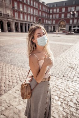 Korunaklı yüz maskesi takan genç turist kadın Coronavirus salgını sonrası İspanya Plaza Belediye Başkanı Madrid 'de mutlu ve heyecanlı bir şekilde Avrupa' da tatilin tadını çıkarıyor. COVID-19 Yeni Normal ve Seyahat.