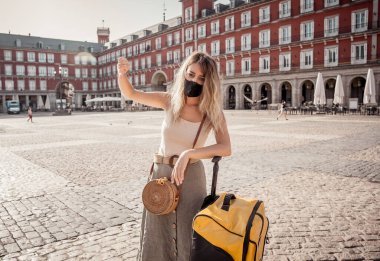 Yüz maskesi ve bavulu olan endişeli kadın turist, kendini izole etme şartları altında strese girdi. Yeni seyahat yönetmeliklerinden etkilenen bir turist. Covid-19 ve uluslararası turizm.