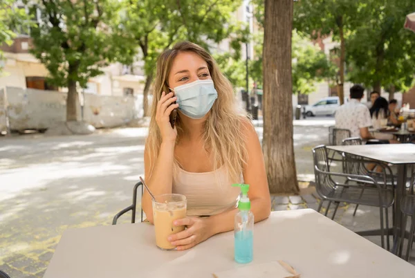 Ung Kvinna Med Skyddsmask Och Handdesinfektionsmedel Videosamtal Med Mobiltelefon Caféet — Stockfoto