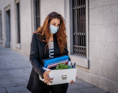 İş bölgesinde tıbbi koruyucu maskeli üzgün bir iş kadını bir kutu ofis çalışanı iş kaybından dolayı depresyonda. Coronavirus iş kesintileri, COVID-19 işsizlik ve ekonomik kriz kavramı.