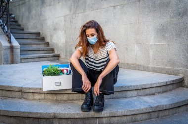İş bölgesinde tıbbi koruyucu maskeli üzgün bir iş kadını bir kutu ofis çalışanı iş kaybından dolayı depresyonda. Coronavirus iş kesintileri, COVID-19 işsizlik ve ekonomik kriz kavramı.