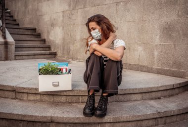 İş bölgesinde tıbbi koruyucu maskeli üzgün bir iş kadını bir kutu ofis çalışanı iş kaybından dolayı depresyonda. Coronavirus iş kesintileri, COVID-19 işsizlik ve ekonomik kriz kavramı.