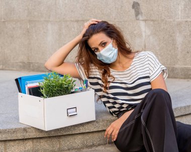İş bölgesinde tıbbi koruyucu maskeli üzgün bir iş kadını bir kutu ofis çalışanı iş kaybından dolayı depresyonda. Coronavirus iş kesintileri, COVID-19 işsizlik ve ekonomik kriz kavramı.