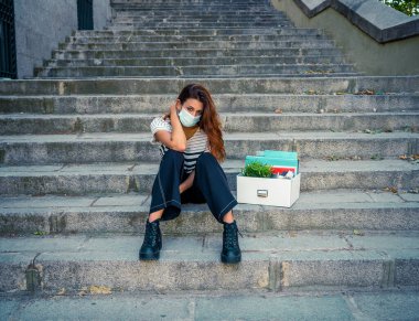 İş bölgesinde tıbbi koruyucu maskeli üzgün bir iş kadını bir kutu ofis çalışanı iş kaybından dolayı depresyonda. Coronavirus iş kesintileri, COVID-19 işsizlik ve ekonomik kriz kavramı.