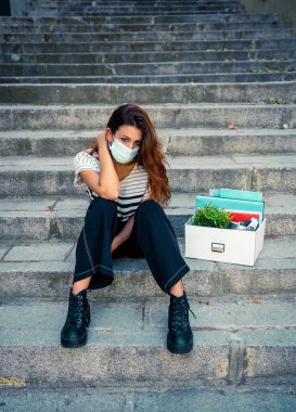 İş bölgesinde tıbbi koruyucu maskeli üzgün bir iş kadını bir kutu ofis çalışanı iş kaybından dolayı depresyonda. Coronavirus iş kesintileri, COVID-19 işsizlik ve ekonomik kriz kavramı.