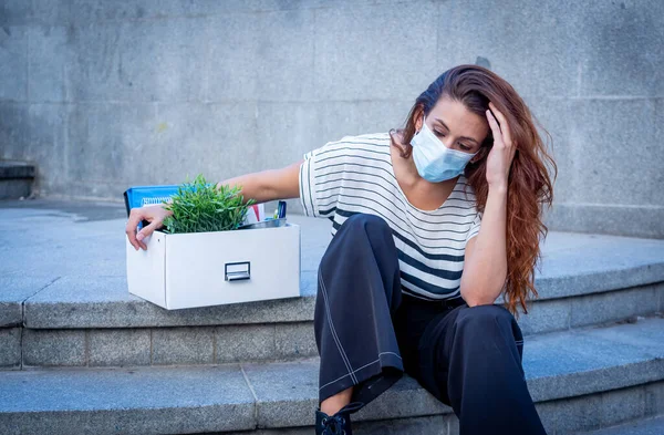 İş bölgesinde tıbbi koruyucu maskeli üzgün bir iş kadını bir kutu ofis çalışanı iş kaybından dolayı depresyonda. Coronavirus iş kesintileri, COVID-19 işsizlik ve ekonomik kriz kavramı.