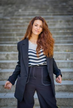 Açık havada, kıvırcık kızıl saçlı ve şehvetli gülüşlü çekici bir kadının portresi var. Doğal güzellikteki şehir geçmişine sahip bir kadın model. Gerçek insanlar, güzellik, moda ve yaşam tarzı.