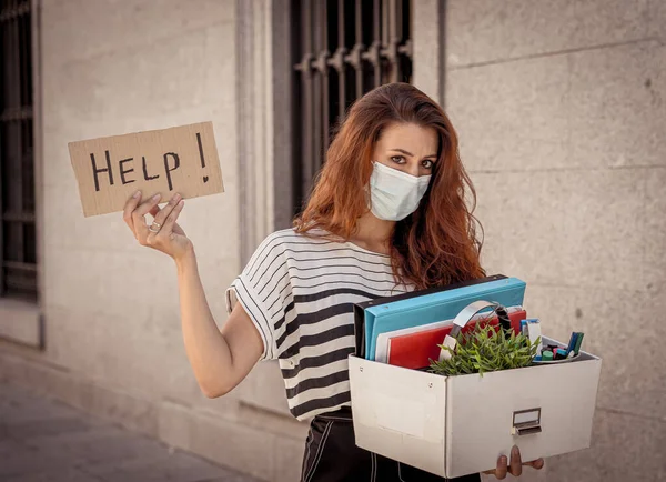 Sad depressed woman wearing face mask just fired from her job holding Help sign and box with personal staff outside office. Coronavirus Outbreak impact in economy, business and unemployment.