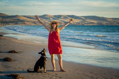 Güzel, olgun bir kadın ve evcil bir köpek uzak, boş bir sahilde deniz kıyısında yürüyor. Emeklilik yaşam tarzını ve köpek dostu turizmi devam ettiren hayvanların Arkadaşlık Yararları.