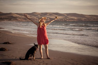 Güzel, olgun bir kadın ve evcil bir köpek uzak, boş bir sahilde deniz kıyısında yürüyor. Emeklilik yaşam tarzını ve köpek dostu turizmi devam ettiren hayvanların Arkadaşlık Yararları.