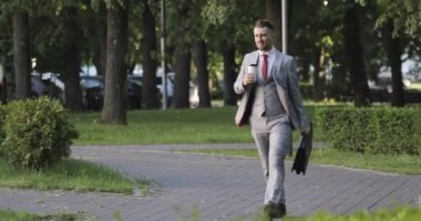 Sakallı bir adam parkta kahve içiyor.