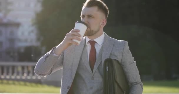 Ein Geschäftsmann im Anzug trinkt Kaffee vor dem Hintergrund von Brunnen in der Stadt. — Stockvideo
