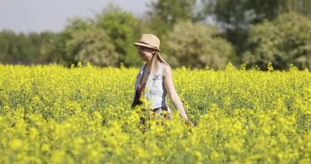 Una joven con sombrero baila en un campo de colza . — Vídeos de Stock