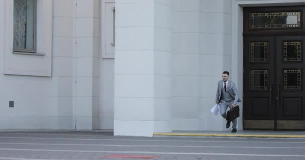 Un rico hombre de negocios con un maletín arroja hojas blancas de papel en la ciudad . — Vídeo de stock