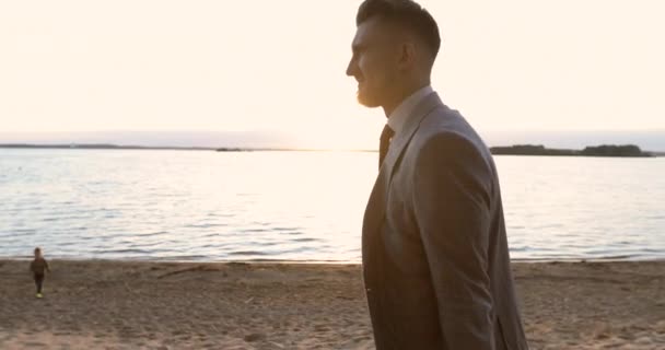 Zakenman in de hand aktetas en wandelen op het strand bij zonsondergang. — Stockvideo