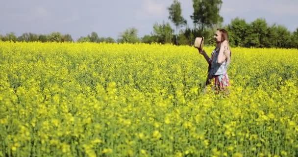Una linda mujer caucásica camina en un campo de colza amarilla en verano . — Vídeos de Stock