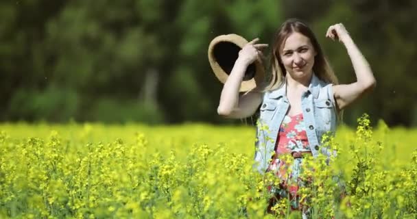 En kvinna i hatt står på ett blommande rapsfält på sommaren.. — Stockvideo