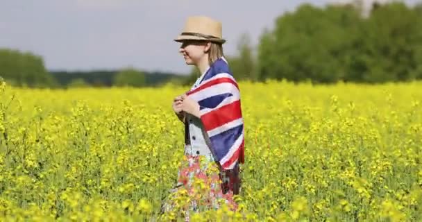 Engelsk flagga på baksidan av en kvinna som går på ett blommande rapsfält på sommaren. — Stockvideo