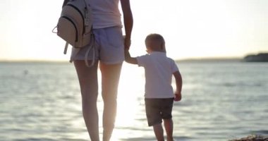 Anne küçük oğlunu elinden tutar ve gün batımının arka planında gölün kıyısında yürür..