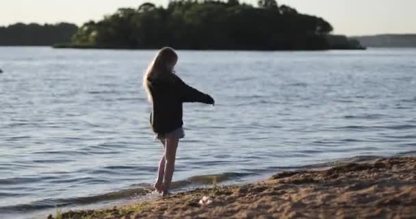 Schöne Mädchen geht barfuß am Ufer des Sees vor dem Hintergrund des Sonnenuntergangs. — Stockvideo