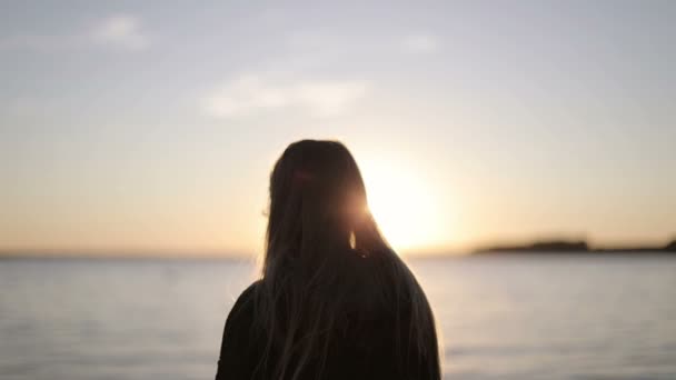 Une fille aux cheveux longs se rend au bord du lac sur un fond de coucher de soleil . — Video