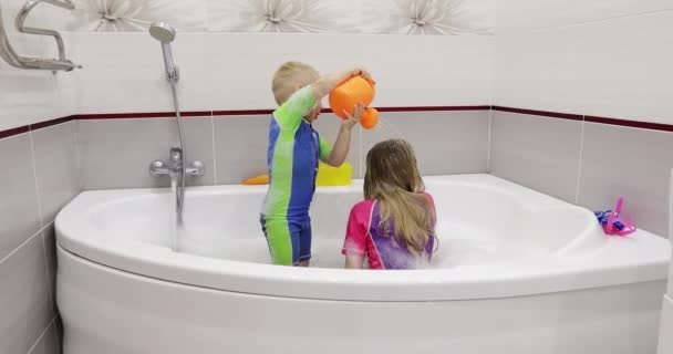 Little boy washing h ad of sister in a bath using plastic watering can. — Stock Video